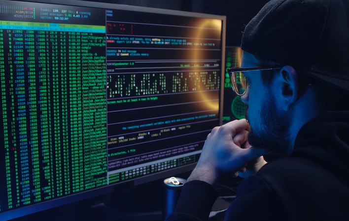 A hacker sits at his computer monitor examining code