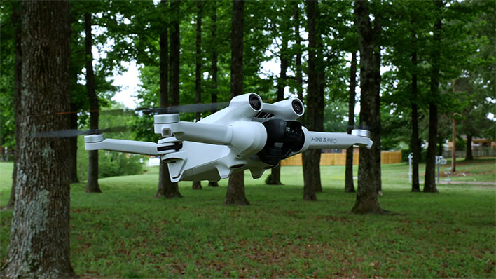 DJI Mini 3 Pro drone flying low in front of trees