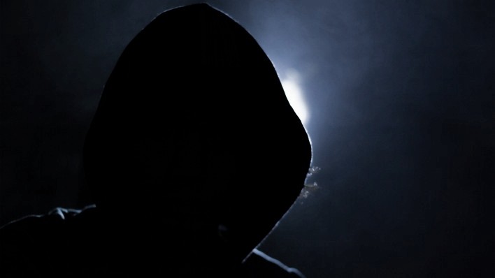 hooded figure shrouded in darkness backlight desaturated news