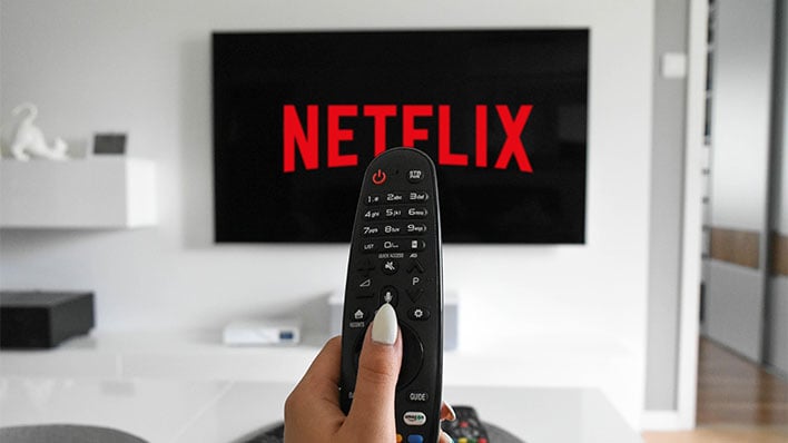 Holding a remote control in a front of a TV with Netflix running.