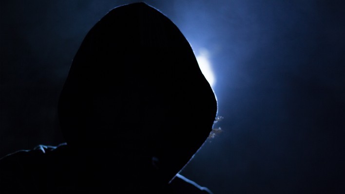 hooded figure shrouded in darkness with backlight news