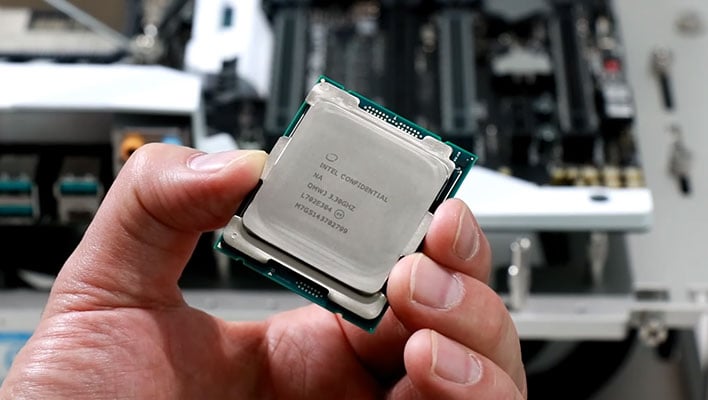 Hand holding an Intel Core i9-7900X processor in front of a motherboard.