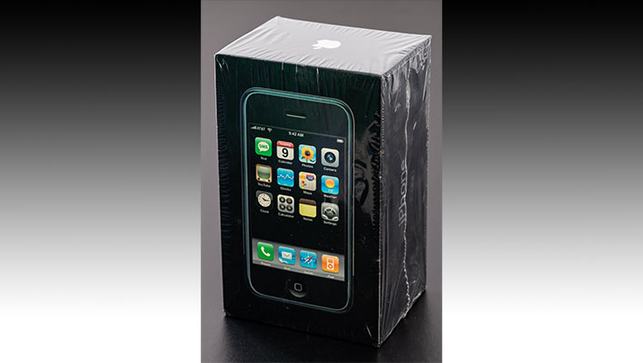 First-gen iPhone in a sealed box on a black and gray gradient background.