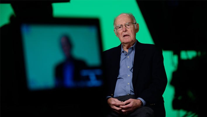 Gordon Moore in his senior years in front of a camera with a green screen behind him.