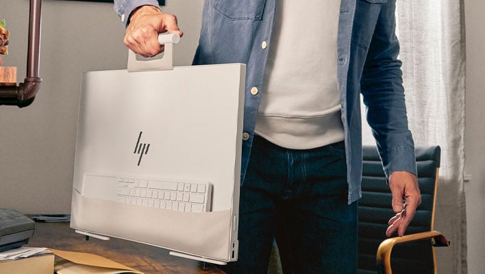 Man holding an HP Envy Move desktop by the handle, with the keyboard tucked in a pouch on the back.