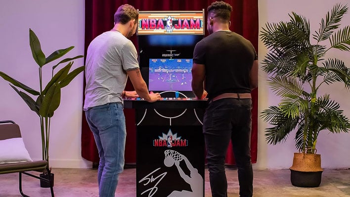 Two people playing an Arcade1Up NBA Jam: Shaq Edition arcade cabinet.