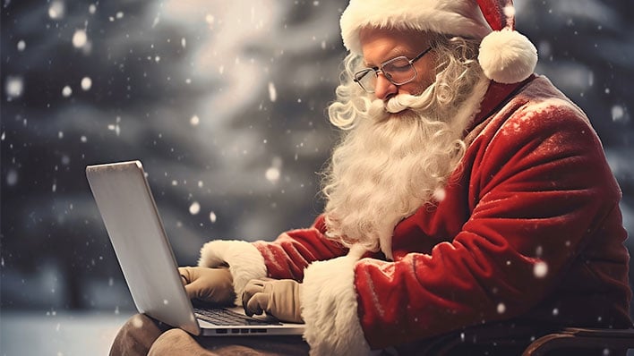 Santa Claus typing on a laptop during a snowfall.