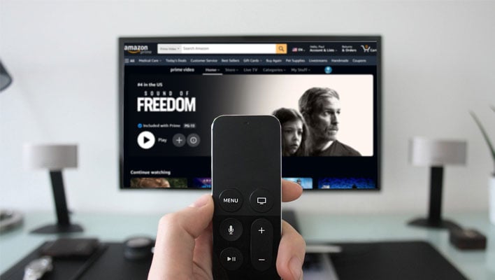 Holding a remote control in front of a TV with Amazon's Prime Video page loaded.