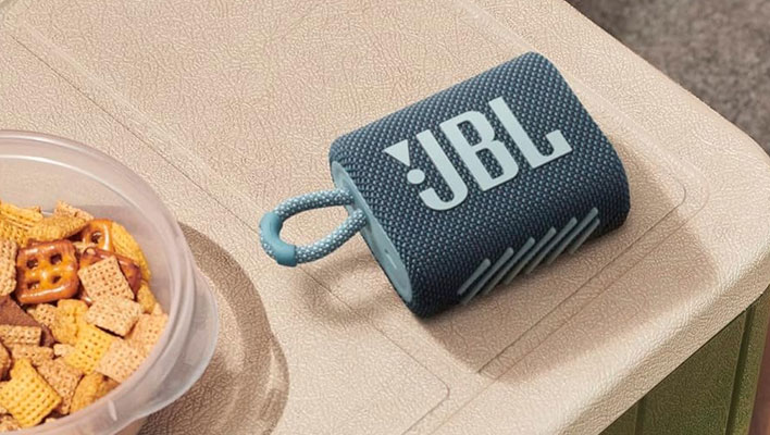 JBL Go 3 portable speaker on a table next to a plastic tin of snacks.