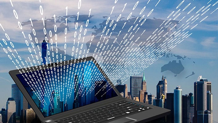 Laptop in front of a city with binary code fililng the sky.