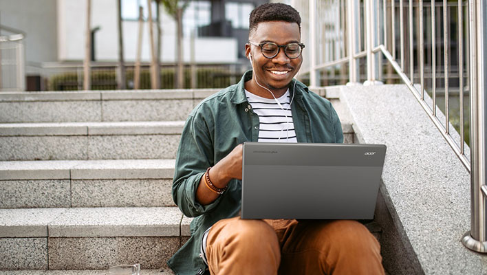 Uomo sorridente sui gradini con un Acer Chromebook Plus 514 in grembo.
