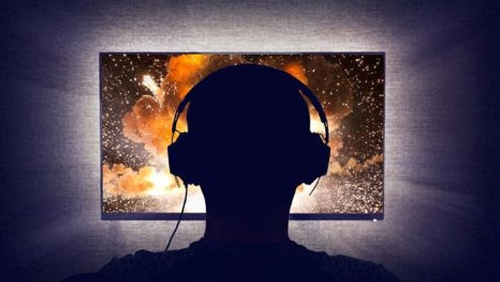 Silhouette of a gamer with headphones staring at a display.