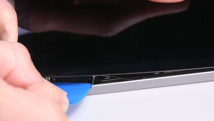 A person using a plastic pick to remove adhesive from an M2 iPad Air.