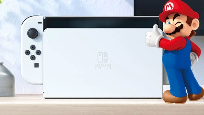 Zbliżenie na białą konsolę Nintendo Switch OLED z mrugającym superimpostem Super Mario z przodu, pokazującym kciuki do góry.