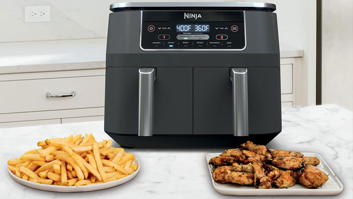 Ninja DZ201 air fryer on a counter next to a plate of French fries and a plate of chicken wings.