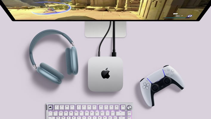 Apple Mac Mini next to a headset and DualSense controller, with a video game on a monitor.