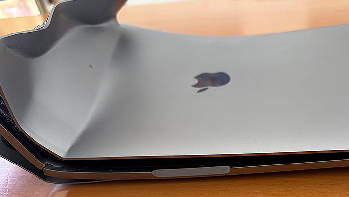 Apple MacBook Pro with damage (badly bent chassis) on a wood table.