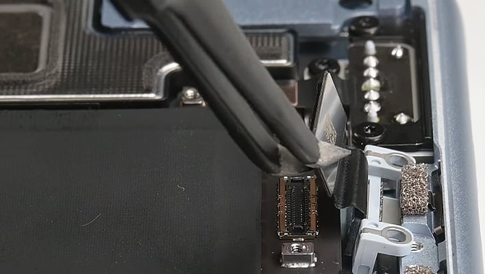 Tweezers tugging at a port in a disassembled MacBook Air.