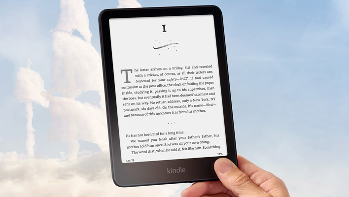Holding a Kindle Paperwhite Signature Edition in front of a blue and cloudy sky.