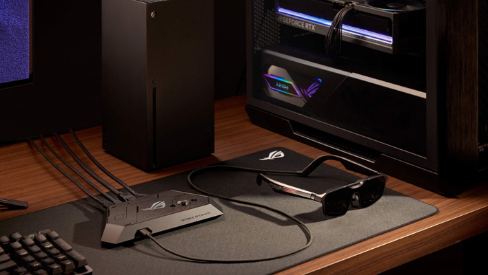 ASUS ROG XREAL R1 glasses connected to a dock on a desk next to an Xbox Series X console and gaming PC.