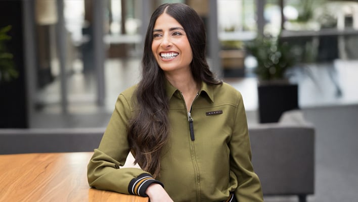 Asha Sharma leaning on a table and smiling.