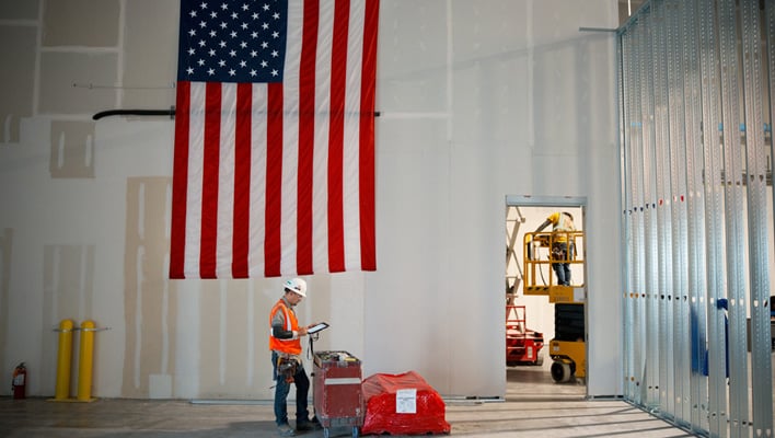 A construction worker inside Apple's unfinished Advanced Manufacturing Center. A USA flag is hanging in the background.