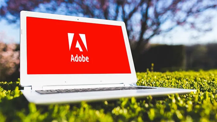 A laptop outside on the grass, with Adobe's logo on the display.
