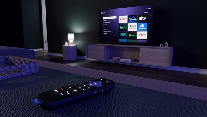 Render of Roku's voice remote (2nd gen) in a dark living room with a Roku TV.