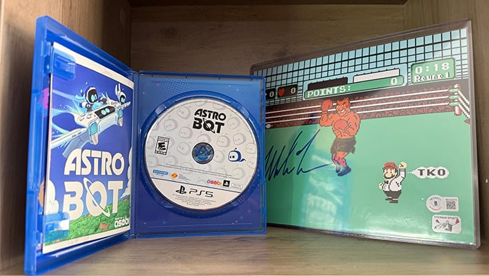 Astro Bot disc in case next to a signed print of Mike Tyson's Punchout.