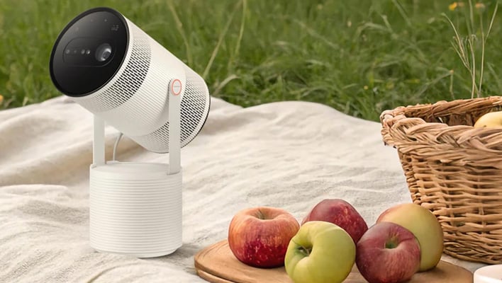Samsung Freestyle+ projector on a blanket next to a picnic basket and apples.