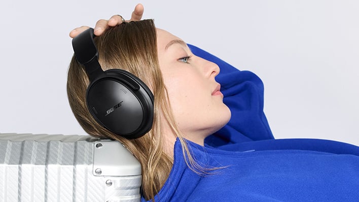 Bose QuietComfort Headphones (2nd Gen) in black. A person is wearing them while laying their head on a suitcase.